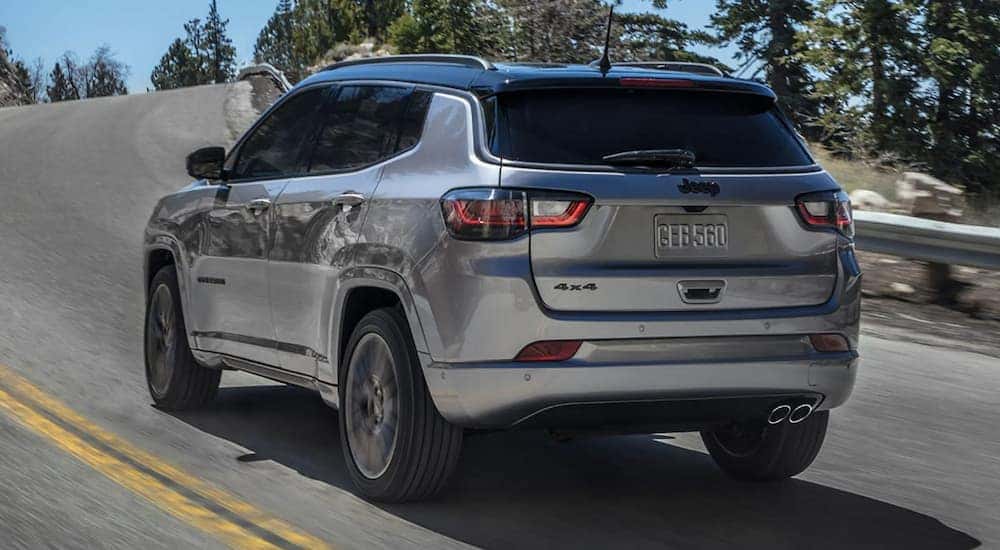 A silver 2022 Jeep Compass is shown from the rear driving on an open road.