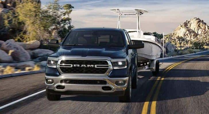 A blue 2023 Ram 1500 is shown towing a boat on an open road.