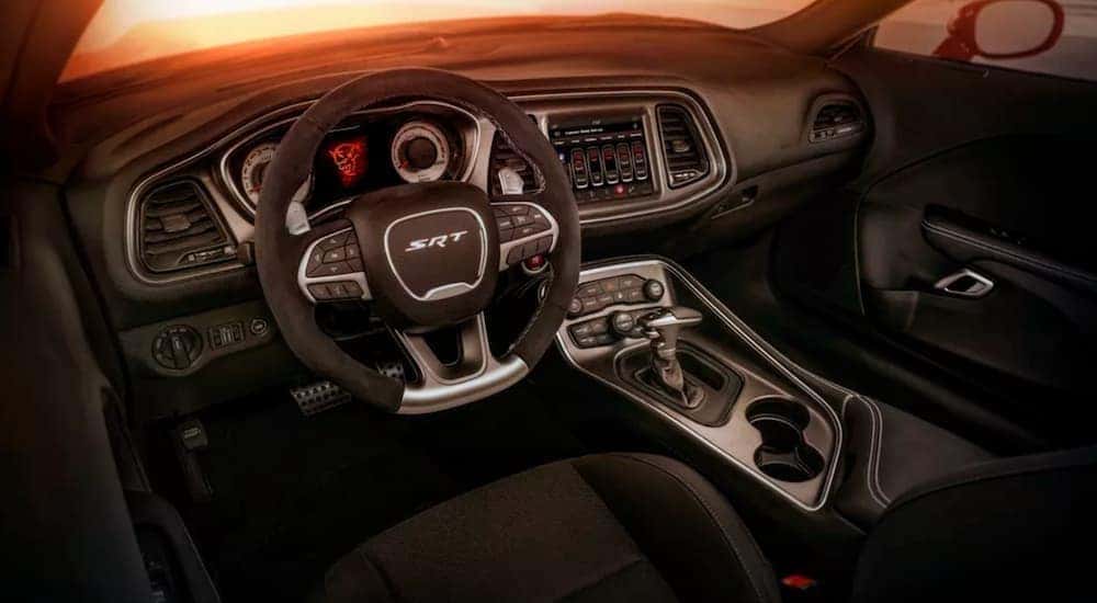 The black interior of a 2018 Dodge Challenger shows the steering wheel and infotainment screen.