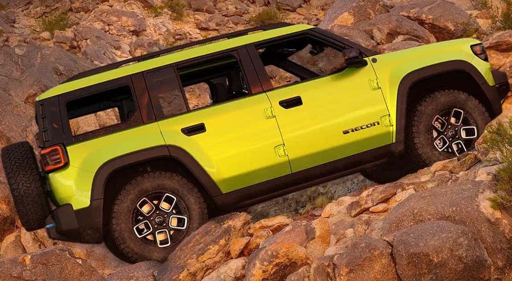 A green 2022 Jeep Recon 4xe is shown from the side while driving on rocks.