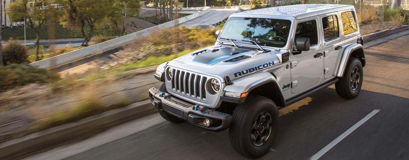 A silver 2023 Jeep Wrangler 4xe is shown driving on an open road.