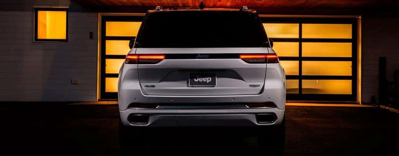 A white 2023 Jeep Grand Cherokee is shown from the rear while parked in a driveway.