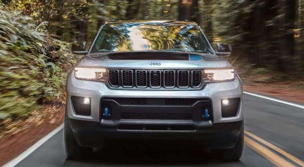 A silver Jeep hybrid, a silver 2022 Jeep Grand Cherokee 4xe, is shown from the front driving on a forest road.