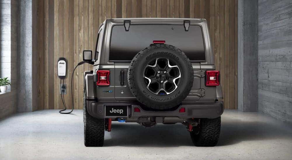 A grey 2022 Jeep Wrangler 4xe is shown from the rear plugged into a home charging station.