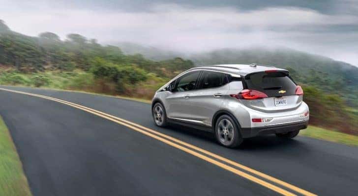 A silver 2020 Chevy Bolt EV is shown from the rear driving on an open road.