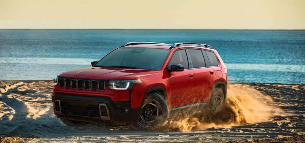 A red 2026 Jeep Cherokee being driven along a beach