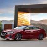 A red 2019 Nissan Maxima is parked in the driveway of a modern house. The maxima is a great choice for driving a Nissan in Huntington Beach.