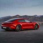 A red 2025 Porsche Taycan GTS overlooking a mountainous cityscape