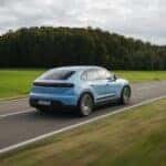 Blue 2025 Porsche Macan electric driving through forested highway