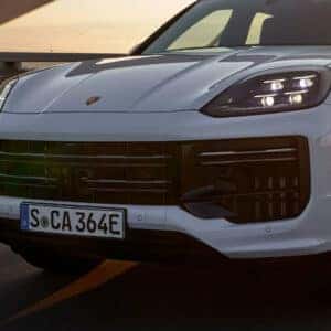 the front view showcasing the front grille and headlights of a porsche cayenne driving over a bridge at sunset