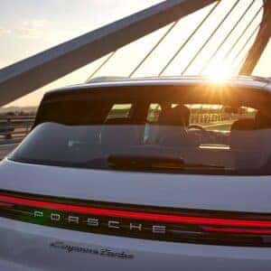 the back exterior of a porsche cayenne driving over a bridge at sunset