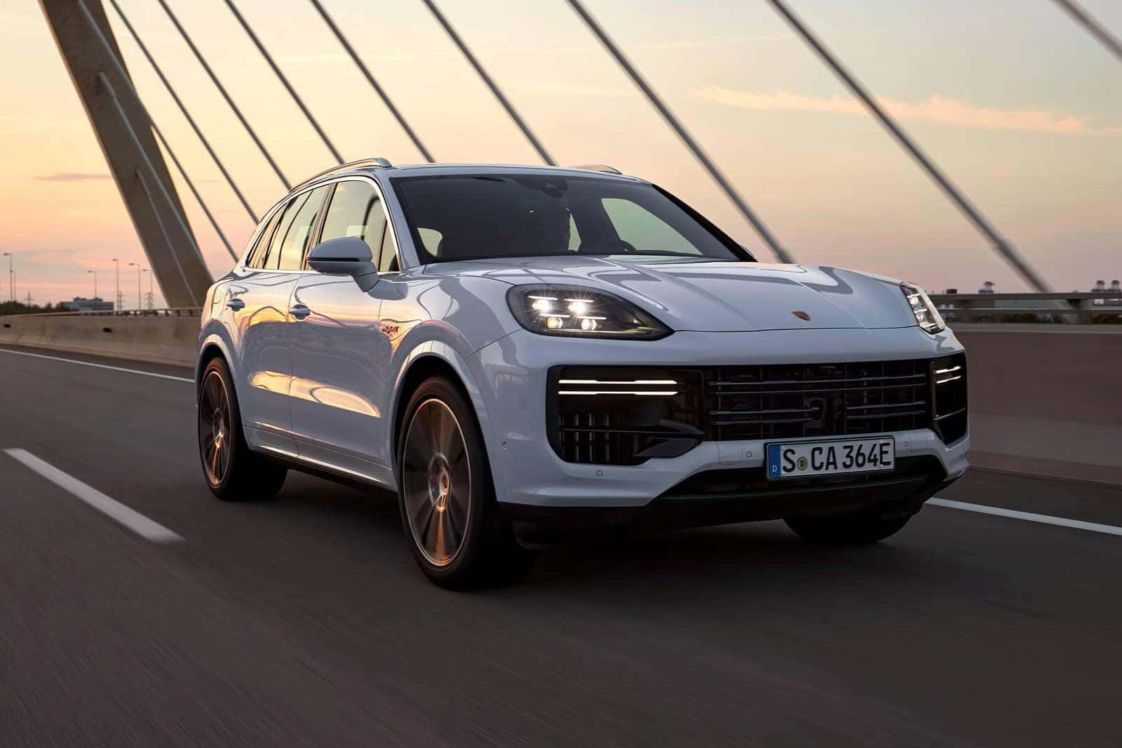a white cayenne suv driving over a bridge at sunset