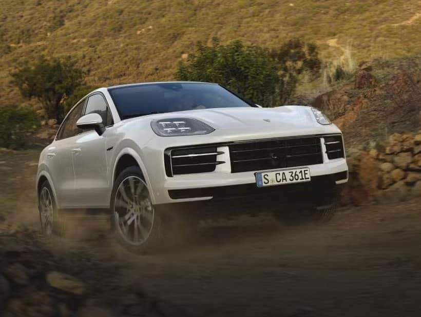 a white porsche cayenne coupe driving on a dirt road in the country