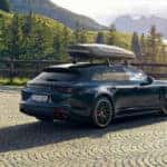 Black Porsche Cayenne with a canoe rack on top of it parked in front a bright mountain scene