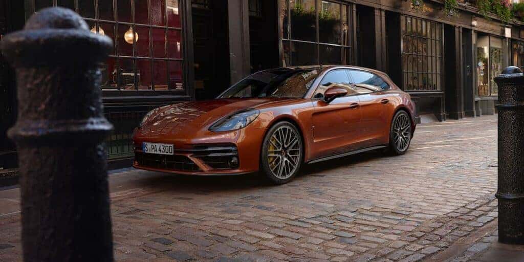 The Porsche Panamera Turbo S parked stylishly in a cobblestone street, highlighting its vibrant orange finish and sporty appeal