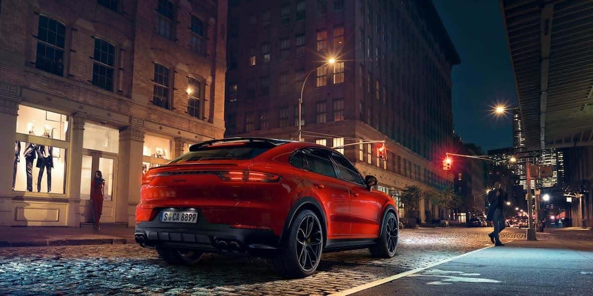 Rear view of a red Porsche Macan on a cobblestone city street at night, emphasizing its sleek design and signature taillights