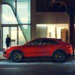 Side profile of the Porsche Cayenne Coupe in red, set against a sleek and modern building backdrop.