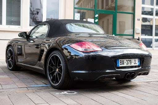 Black porsche 718 boxster parked over a handdicapped spot.