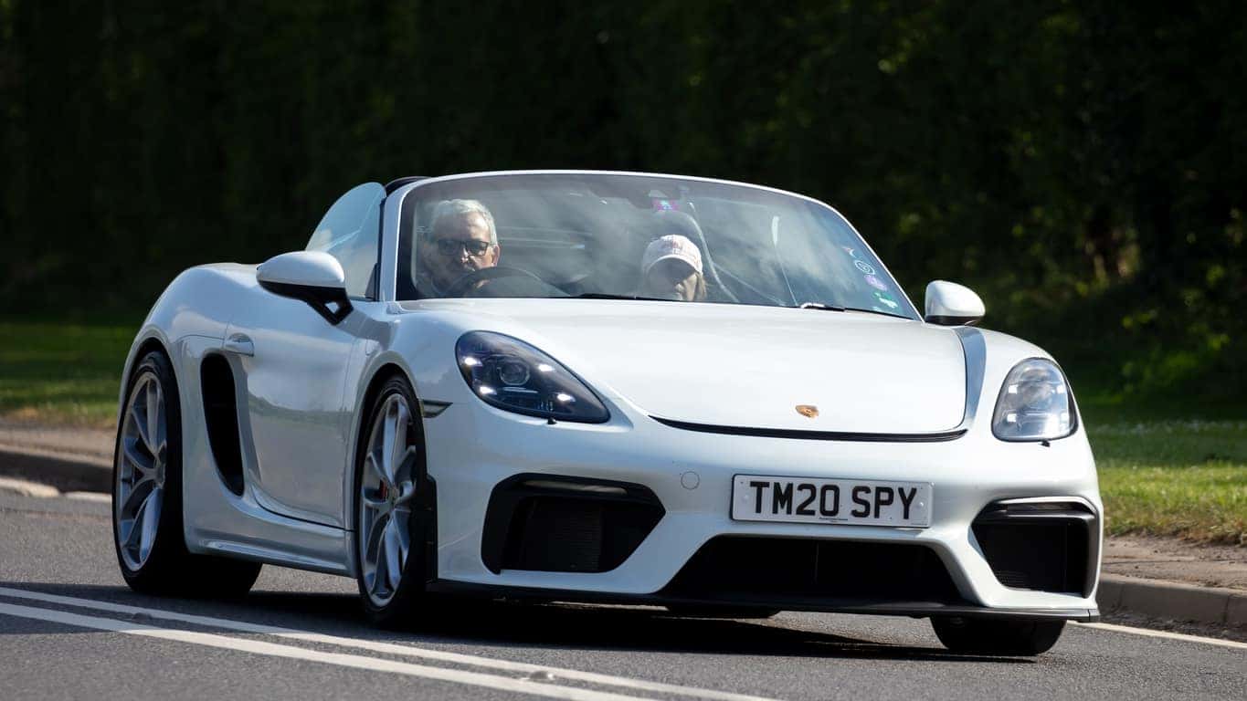 An all white Porsche 718 Spyder driving down a highway with an older couple in the front seat.