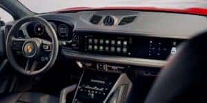 The interior of a Porsche Cayenne featuring a luxurious dashboard with a sleek, modern design. The image highlights the digital instrument cluster and a wide touchscreen display, showcasing advanced technology and premium materials, providing insight into the differences in interior features when comparing the Porsche Macan vs Cayenne.