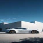 2025 Porsche 911 sports car in white, showcasing its sleek aerodynamic design, distinctive silhouette, and golden wheels against a modern architectural backdrop