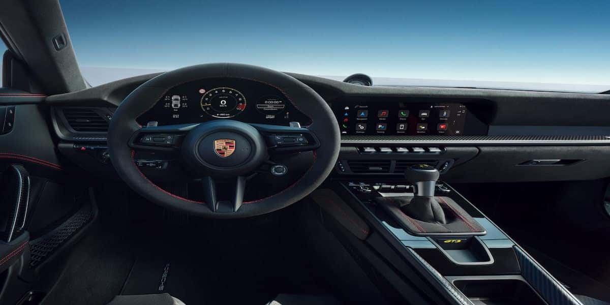 2025 Porsche 911 GTS interior highlighting the Alcantara steering wheel, advanced digital dashboard, manual transmission shifter, and carbon fiber details for a luxurious and sporty driving experience.