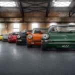 The evolution of Porsche 911 generations displayed in an industrial setting, highlighting the transition from the classic green 911 model to its contemporary counterparts, illustrating decades of design and performance excellence.