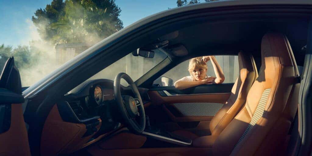 Interior view of the Porsche 911 Sport Classic with cognac leather seats and retro-inspired houndstooth upholstery, featuring a woman leaning on the window for a nostalgic feel.