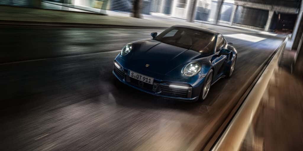 A blue Porsche 911 Turbo S speeding through a modern city at night, showcasing its aerodynamic design and high-performance capabilities.