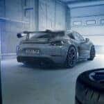 Rear view of a Porsche GT4 RS in a garage, showcasing its large wing, dual exhaust, and motorsport-inspired design, surrounded by racing tires and tools.