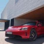 Front view of a red Porsche Taycan GTS parked outside a modern luxury home, showcasing the sleek electric sports car design.