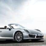 Silver Porsche 911 convertible parked on an open road, illustrating when was the Porsche 911 made with iconic styling.