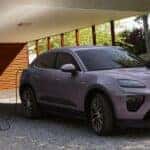Porsche ev SUV in light purple charging at home while a woman places a bag on the hood in a modern residential setting.
