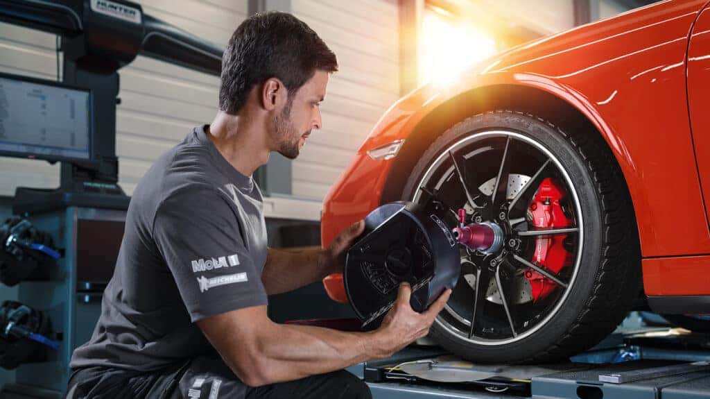 Photo of a Certified Porsche Technician working on the wheel of a sports car. Used to illustrate the article - The Benefits of Servicing Your Porsche at a Certified Dealership - Craftsmanship, Expertise, and Resale Value.