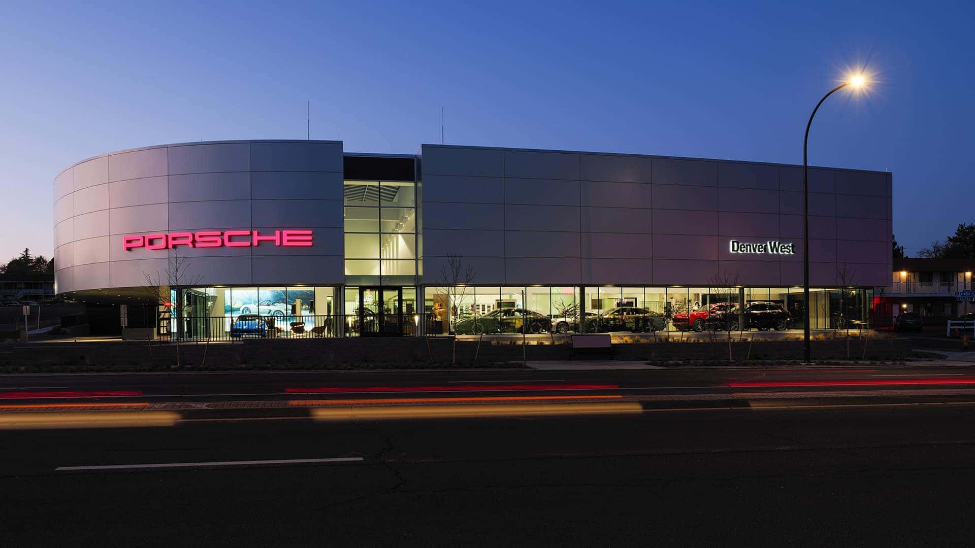 Porsche Denver West as seen from across Colfax Ave. with blurred vehicle lights in the foreground.