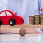 Man's Hand Placing Coin On Top Of The Stack Coins And Red Car Over Seesaw
