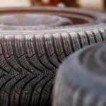 New tire laying on the pavement near the mechanic ready to replace the one on a car.