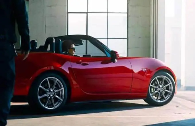 A red Mazda convertible is driving out of a garage