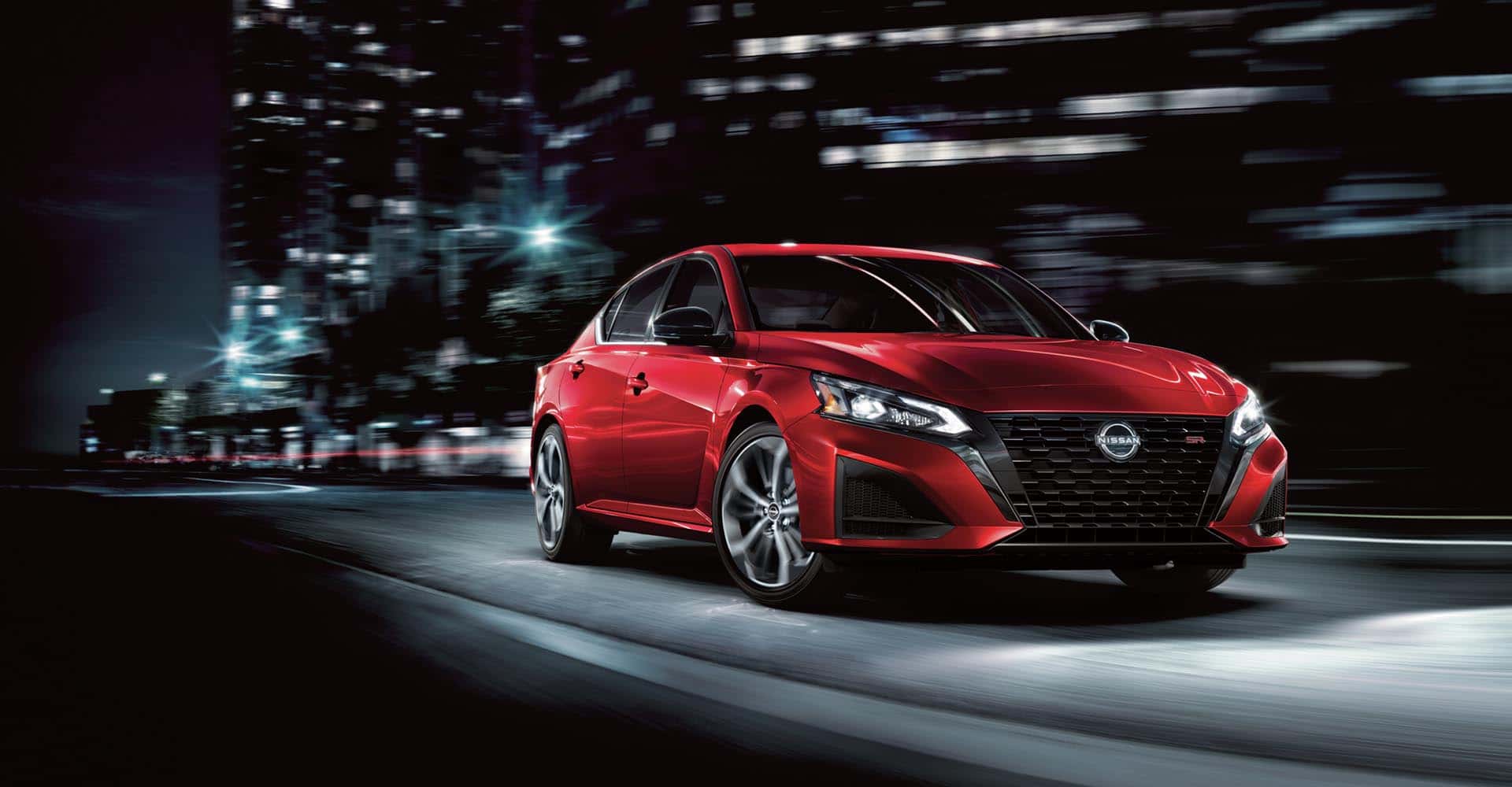 Red 2025 Nissan Altima drtiving down city street at night
