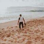 man walking on beach with shoes in hand