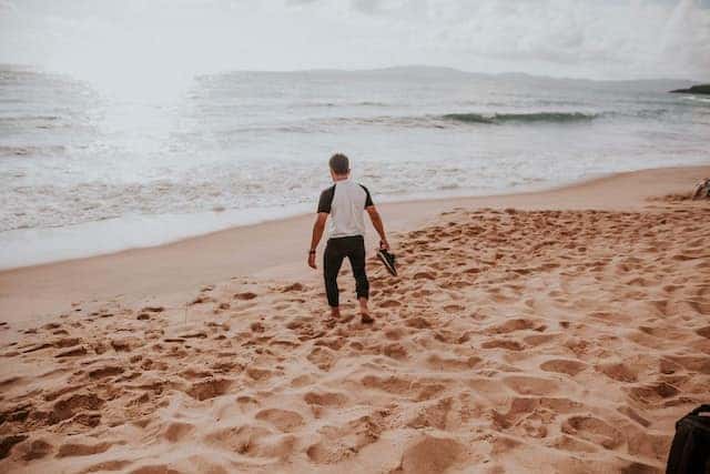 man walking on beach with shoes in hand