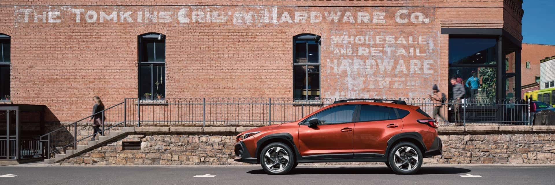 Orange 2025 Subaru Crosstrek parked on the street in front of an old brick building with painted signage