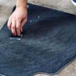 Hand cleaning carpeted car floor mat with brush