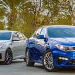 Two Kia Optima models parked beneath palm trees