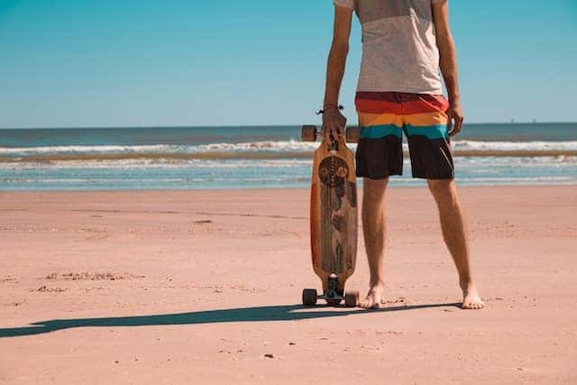 man holding skateboard standing on beach